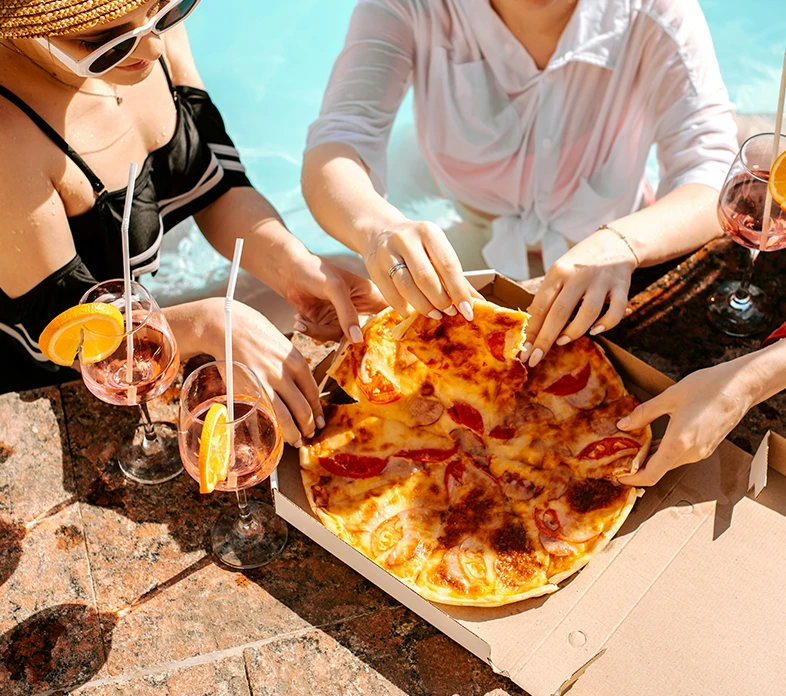 Eine Gruppe von Frauen isst eine Lieferpizza Pizza am Pool